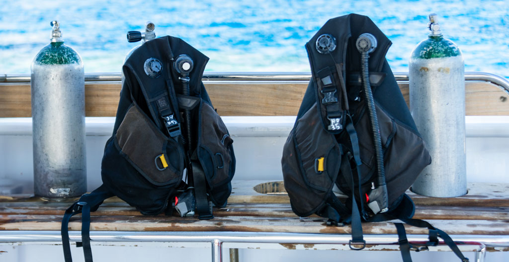 Trois gilets de plongée différents alignés sur un banc de préparation en bord de mer